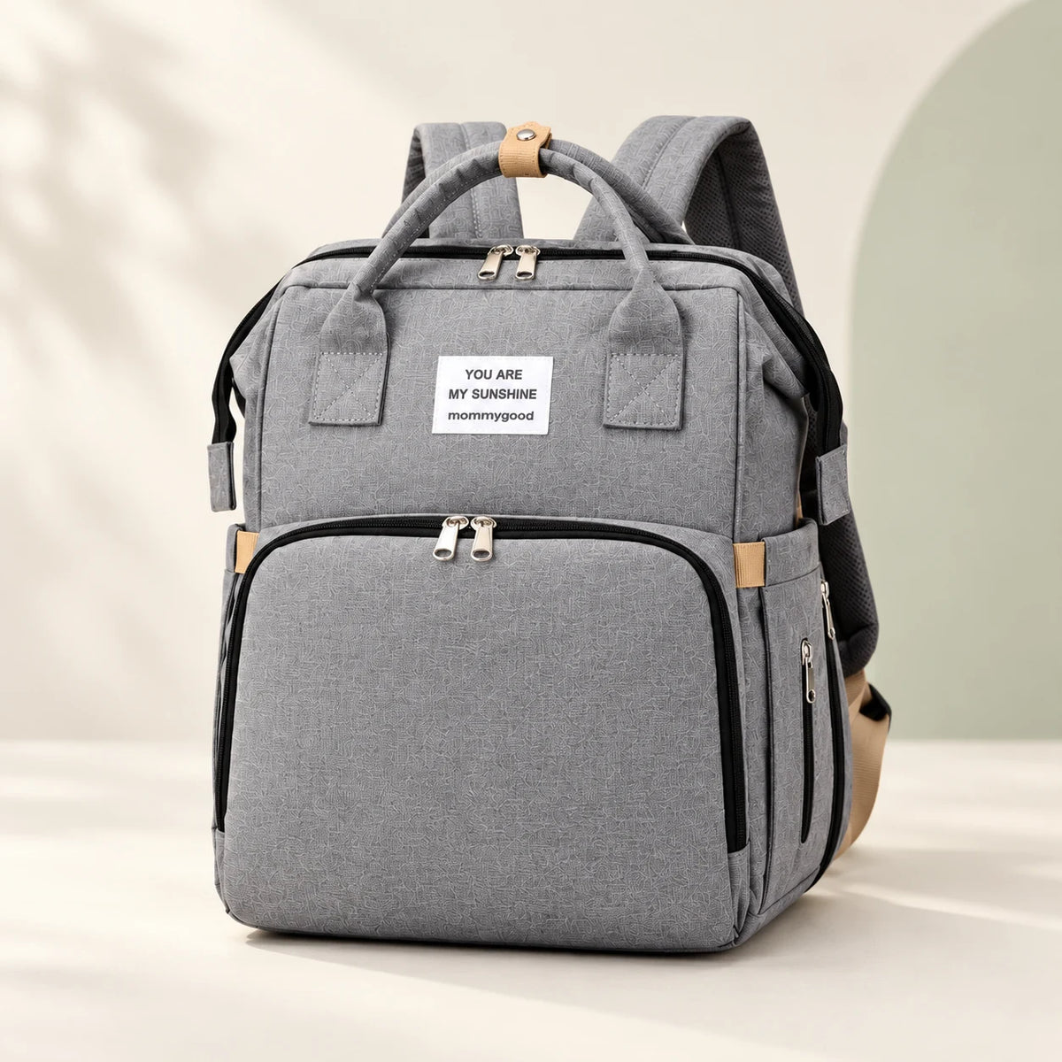Gray convertible diaper backpack with beige accents, shown closed against a warm ivory background.